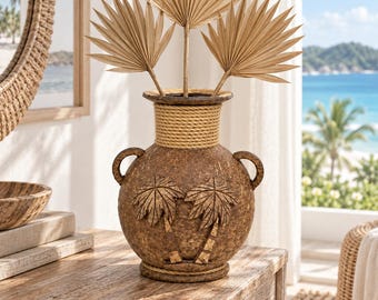 May include: A brown textured vase with two side handles, featuring a carved palm tree design on the front. The neck and base are wrapped in thick tan rope. Three dried fan-shaped palm leaves are arranged inside the vase as a decorative display.
