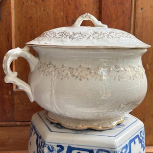 May include: A white ceramic mug with a black handle and the text "But First, Coffee" in a bold, black font. The mug is set against a blurred background, suggesting a cozy setting.