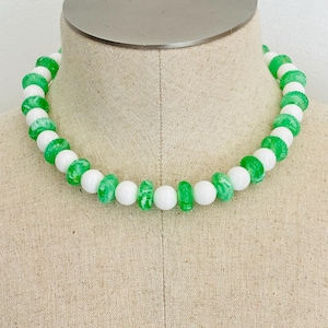 Puede incluir: Un collar de cuentas con cuentas blancas y verdes alternas. Las cuentas verdes tienen un aspecto veteado. El collar se exhibe en un maniquí. Este es un accesorio de moda.