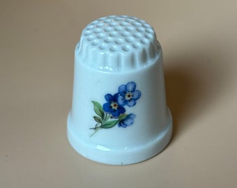 Peut inclure: Dé à coudre en céramique blanche avec un motif de fleurs bleues myosotis.