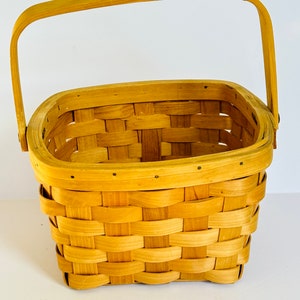 Peut inclure: Un panier rectangulaire en bois tressé avec une seule poignée. Le panier est en bois naturel et a une couleur brun clair.