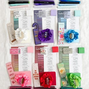 May include: Six stationery sets arranged in a grid, each featuring a book tracker sheet, a bookmark, a satin scrunchie, a roll of washi tape, a sticky note pad, and three pens in coordinating colours. The items display various themes and text.