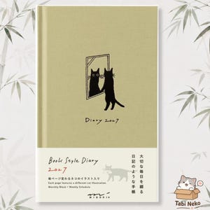 May include: A light olive green 2027 diary with a black line drawing of a cat looking into a mirror. The cover features the text Diary 2027. A white paper band at the bottom includes the text Book Style Diary 2027, Japanese characters, and a cat.