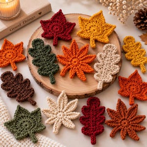 Könnte beinhalten: Eine Sammlung gehäkelter Herbstblätter in verschiedenen Formen und Farben, darunter Rot, Orange, Gelb, Grün, Braun und Creme. Die Blätter sind auf einem runden Holzbrett angeordnet, einige liegen auf der Fläche um das Brett herum.