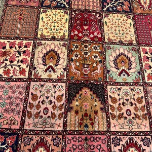 May include: A rectangular area rug featuring a grid of square panels, each displaying intricate floral and botanical motifs in shades of pink, red, cream, brown, and green. The design includes stylized trees, vases, and birds within a dark border.
