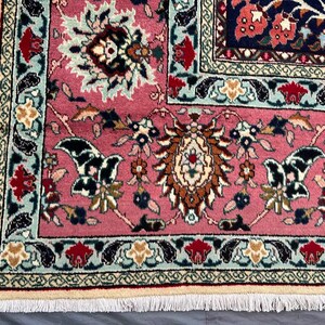 May include: A rectangular area rug featuring a vibrant pink field with intricate floral and botanical motifs in shades of navy blue, cream, red, and light blue. The rug has a detailed decorative border and a cream-colored fringe along the edge.