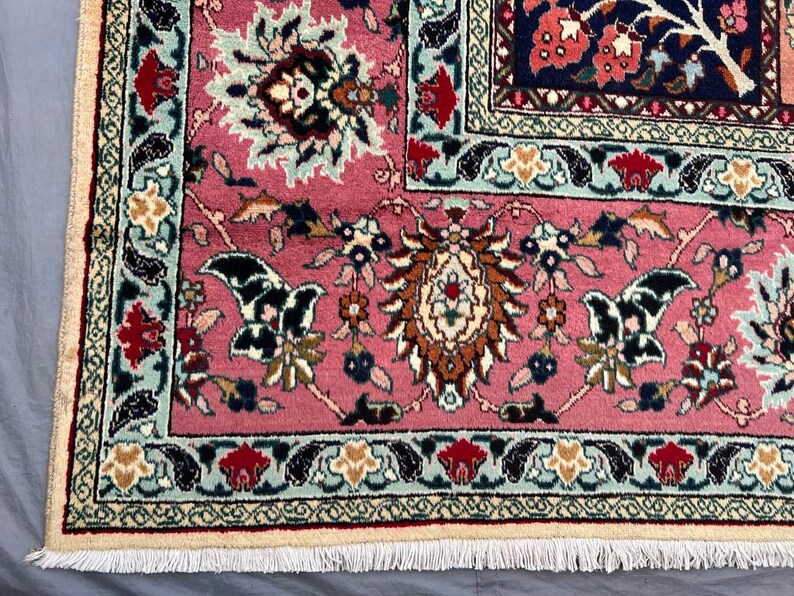 May include: A rectangular area rug featuring a vibrant pink field with intricate floral and botanical motifs in shades of navy blue, cream, red, and light blue. The rug has a detailed decorative border and a cream-colored fringe along the edge.