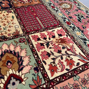 May include: A rectangular area rug featuring a grid of square panels, each decorated with intricate floral and bird motifs in shades of pink, cream, sage green, and deep red. The border displays a dense pattern of stylized blossoms and vines.
