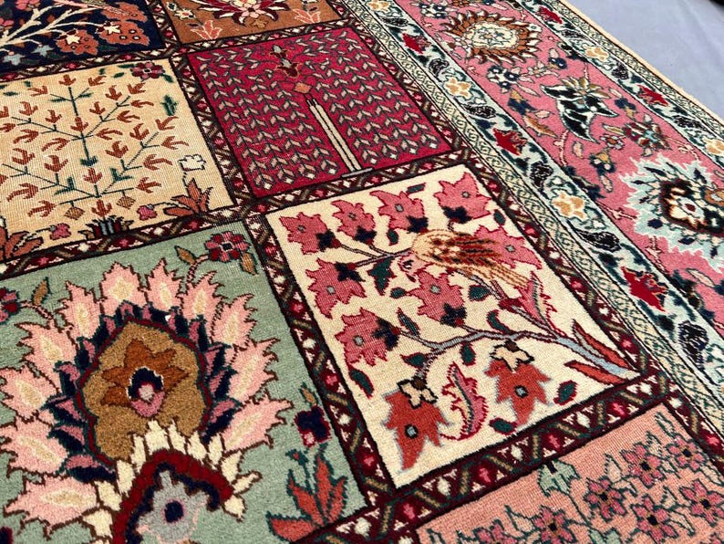 May include: A rectangular area rug featuring a grid of square panels, each decorated with intricate floral and bird motifs in shades of pink, cream, sage green, and deep red. The border displays a dense pattern of stylized blossoms and vines.