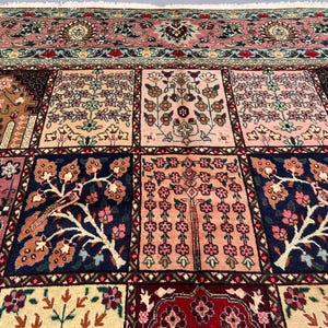 May include: A rectangular area rug featuring a grid of square panels, each decorated with intricate floral and tree motifs in shades of pink, navy blue, cream, and brown. The rug includes a wide, detailed border with repeating patterns and fringe.