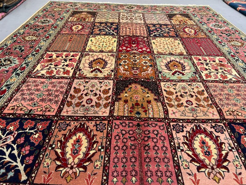 May include: A large rectangular area rug featuring a grid of square panels, each decorated with intricate floral, botanical, and architectural motifs in shades of pink, red, navy blue, cream, and gold, finished with a thin fringe along the edge.