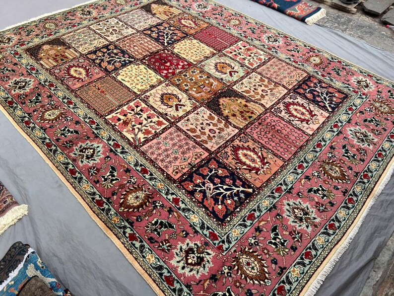 May include: A rectangular area rug featuring a patchwork design of various floral and botanical motifs in shades of pink, cream, deep red, and navy blue. The rug has a wide, ornate border with intricate patterns and a fringe along the edges.
