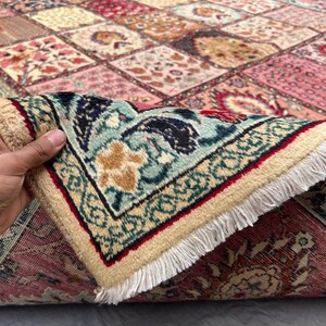 May include: A rectangular area rug featuring a patchwork design of various floral and geometric patterns in shades of pink, red, blue, and cream. The rug has a thick, light-colored fringe along the edge and a dense, woven pile construction.