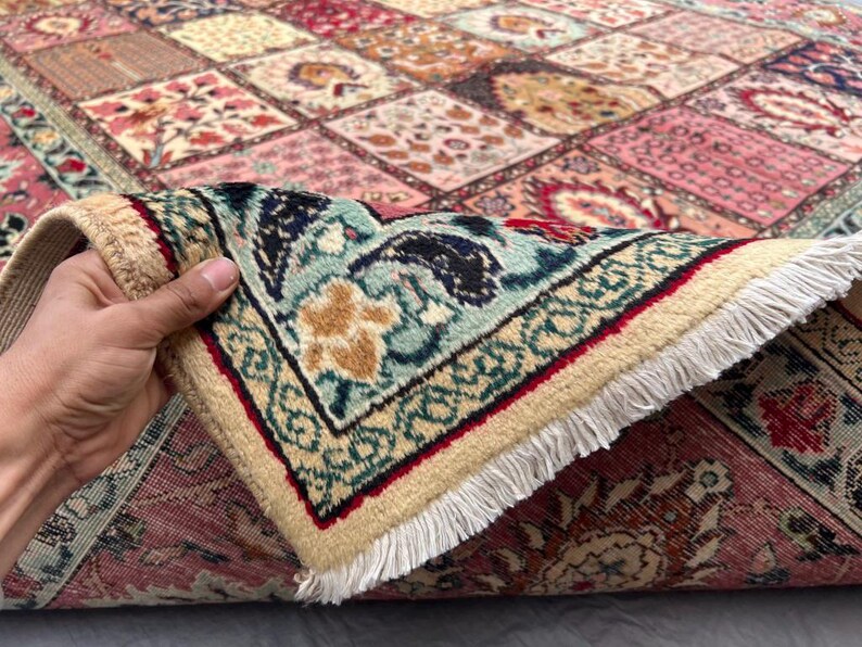 May include: A rectangular area rug featuring a patchwork design of various floral and geometric patterns in shades of pink, red, blue, and cream. The rug has a thick, light-colored fringe along the edge and a dense, woven pile construction.