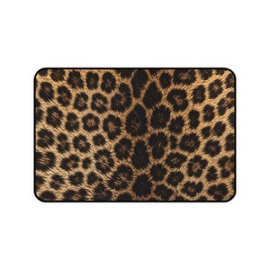 Könnte beinhalten: Eine rechteckige Matte mit einem sich wiederholenden Leopardenmuster. Das Design besteht aus dunkelbraunen und schwarzen unregelmäßigen Flecken auf einem warmen, goldbraunen Hintergrund. Die gesamte Fläche ist von einem dünnen, schwarzen Rand umgeben.