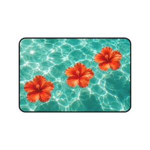 Könnte beinhalten: Eine rechteckige Schreibtischunterlage mit einem lebendigen Grafikdruck von drei leuchtend orangefarbenen Hibiskusblüten, die auf klarem, kräuselndem türkisfarbenem Wasser schwimmen. Die Oberfläche zeigt ein kontrastreiches Licht- und Schattenspiel.