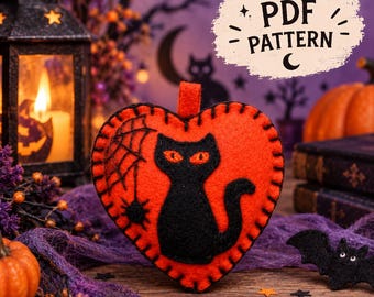 Puede incluir: Un adorno de fieltro en forma de corazón de color naranja brillante con la silueta de un gato negro y un diseño de telaraña. Los bordes están cosidos con hilo negro. Un gráfico blanco en forma de nube muestra el texto PDF PATTERN.