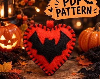 Puede incluir: Un adorno de corazón de fieltro rojo con una aplicación de murciélago negro en el centro y costuras de festón negras en los bordes. Un gráfico naranja en la esquina superior derecha muestra el texto PDF PATTERN con un icono de murciélago.