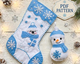 Puede incluir: Un calcetín navideño de fieltro blanco y azul claro con un oso polar que lleva gorro y bufanda mientras sostiene un regalo, junto a un adorno de muñeco de nieve a juego y un cartel que dice PDF PATTERN con copos de nieve.