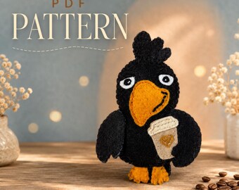 Puede incluir: Un proyecto de manualidades en fieltro que muestra un pájaro negro con un gran pico naranja, ojos blancos y patas naranjas, sosteniendo una taza de café beige con un corazón. El texto PDF PATTERN aparece sobre el pájaro de fieltro cosido.