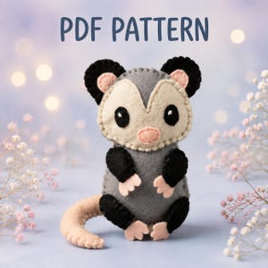 Puede incluir: Un peluche de fieltro con forma de zarigüeya que presenta un cuerpo gris, orejas y extremidades negras, y una cara color crema con una nariz rosa. El juguete tiene costuras visibles en los bordes. El texto PDF PATTERN aparece arriba.