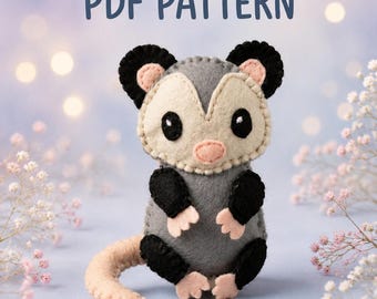 Puede incluir: Un peluche de fieltro con forma de zarigüeya que presenta un cuerpo gris, orejas y extremidades negras, y una cara color crema con una nariz rosa. El juguete tiene costuras visibles en los bordes. El texto PDF PATTERN aparece arriba.