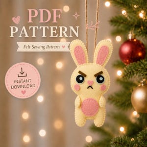 May include: A felt sewing pattern for a hanging ornament featuring a pale yellow rabbit with pink inner ears, cheeks, and belly. The rabbit has an angry expression with dark eyebrows and blue eyes. Text reads PDF PATTERN, Felt Sewing Pattern, and INSTANT DOWNLOAD.