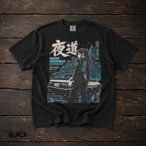 Puede incluir: Una camiseta negra de manga corta con un estampado gráfico de una persona de pie frente a un coche deportivo con un horizonte urbano de fondo. El diseño incluye texto en japonés, las palabras Neon Highway y detalles en azul y blanco.