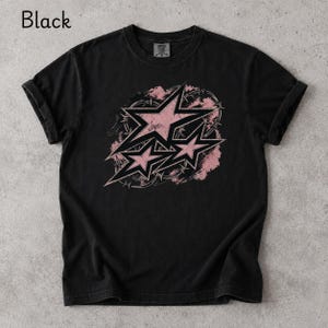 May include: A black short-sleeve t-shirt featuring a graphic print of three pink stars layered over a circular barbed wire design. The stars have a distressed texture and black outlines. The word Black is printed in the top left corner.
