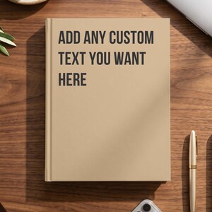 May include: A tan hardcover notebook with black text printed on the front cover that reads, ADD ANY CUSTOM TEXT YOU WANT HERE. The notebook features a clean, solid-colored surface and a sturdy spine, providing a blank canvas for personalization.