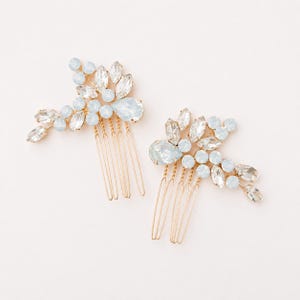 May include: Two hair combs featuring gold-toned metal teeth and decorative floral arrangements. Each piece is adorned with clear marquise-cut crystals and round, pale blue opalescent stones arranged in a cluster pattern on the top section.