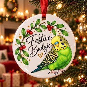 Könnte beinhalten: Ein rundes, weißes Keramikornament mit einer Illustration eines grünen und gelben Wellensittichs, einem Stechpalmenzweig mit roten und weißen Beeren sowie dem Text "Festive Budgie" und einem kleinen goldenen Herz. Ein rotes Band dient zum Aufhängen.