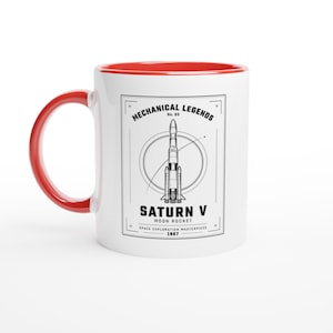 May include: A white ceramic mug with a bright red handle and interior rim. The front features a black graphic of a Saturn V rocket inside a circular frame, with the text "MECHANICAL LEGENDS No. 03 SATURN V MOON ROCKET SPACE EXPLORATION MASTERPIECE 1967."
