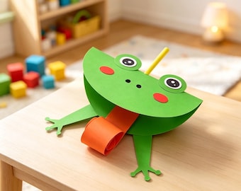 May include: A green paper craft frog with large white and black eyes, red circular cheeks, and a long orange curled tongue. The frog features a yellow stick protruding from the top and two green paper legs extending from the sides of the body.