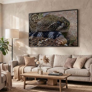 Op de afbeelding: Een rechthoekige wandkunstprint met een gedetailleerde close-up van de kop van een ratelslang met gestructureerde bruine en tan schubben, donkere ogen en een opvallende ratel, ingelijst in een dunne zwarte lijst boven een bank in de woonkamer.