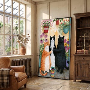 Op de afbeelding: Een ingelijste verticale muurkunstprint met drie katten die samen staan. Een oranje cyperse kat, een zwart-witte tuxedo-kat en een effen zwarte kat zijn afgebeeld. De katten zijn omringd door kleurrijke potbloemen en een kleine mok met patronen.