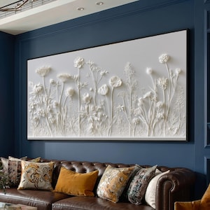 May include: A large rectangular wall art piece featuring a white relief sculpture of various wildflowers and grasses. The artwork displays intricate, raised floral textures against a flat white background, framed in a thin black border.