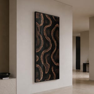 May include: A tall, rectangular wall art piece featuring a black and copper-toned snakeskin pattern. The artwork is enclosed in a thin black frame and displays a repeating, organic, wavy texture that mimics the appearance of reptile scales.