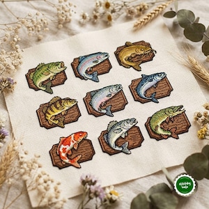 May include: A cross-stitch embroidery on off-white fabric featuring eight distinct fish mounted on individual brown wooden plaques. The fish include a green bass, blue trout, yellow catfish, yellow perch, salmon, mackerel, orange koi, and a gray pike.