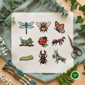 May include: A square piece of white Aida fabric featuring a cross-stitch pattern of nine insects arranged in a grid, including a dragonfly, bee, butterfly, grasshopper, ladybug, ant, caterpillar, stag beetle, and praying mantis.