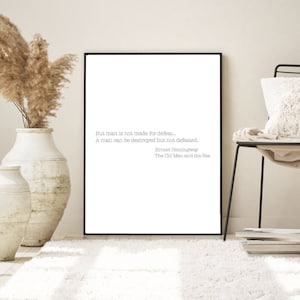 May include: A black framed print with a white background and a quote from Ernest Hemingway's "The Old Man and the Sea" that reads: "But man is not made for defeat... A man can be destroyed but not defeated."