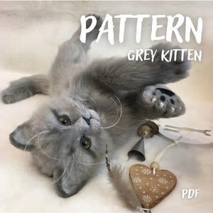 May include: A plush grey kitten toy lying on its back with amber eyes and long white whiskers. The text PATTERN GREY KITTEN is visible at the top, and PDF is at the bottom right. A wooden heart ornament with snowflake patterns is nearby.