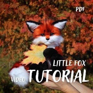 May include: A plush fox toy with orange, black, and white fur holding a yellow and orange maple leaf. The text PDF, LITTLE FOX, and VIDEO TUTORIAL are printed on the image. The fox has dark eyes, pointed ears, and a white-tipped tail.