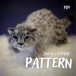 May include: A plush snow leopard toy with grey and white fur featuring dark spots, blue eyes, and a long tail. The text PDF SNOW LEOPARD PATTERN is displayed in white lettering over the image of the toy, which is positioned in a crouching stance.