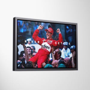 May include: A framed horizontal wall art print featuring a photograph of a race car driver in a red racing suit with arms raised in celebration, surrounded by a crowd. The text NEVER SETTLE is printed in white capital letters across the center.