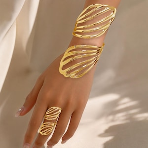 May include: A set of gold-toned jewelry consisting of two wide, open-work cuff bracelets with a curved, layered wire design and a matching open-work ring featuring a similar layered, curved wire pattern on the finger.