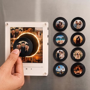 Può includere: Una cornice portafoto quadrata in acrilico con un centro circolare illuminato e una collezione di otto magneti neri circolari, ognuno dei quali presenta una fotografia diversa. La cornice mostra una griglia di immagini e i magneti mostrano vari momenti personali.
