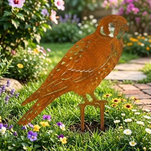 May include: A rust-coloured metal garden stake shaped like a falcon in profile. The silhouette features cut-out details representing feathers and facial markings, with two sturdy metal prongs at the base for insertion into the ground.