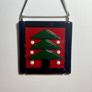 May include: A red and green glass Christmas tree bauble with a black frame and white baubles. The bauble has a black string for hanging.
