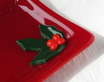 May include: A red glass dish with a green holly leaf and red berries design.